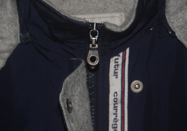 Puede incluir: Una chaqueta azul marino con una cremallera gris y una franja blanca y roja con el texto "futur courr&egrave;ge" en el lado derecho.