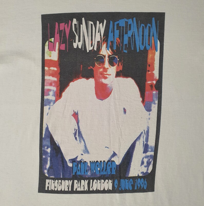 Pode incluir: Uma camiseta vintage de concerto com uma imagem em preto e branco de Paul Weller, com o texto "Lazy Sunday Afternoon" em letras azuis e rosas. O texto "Finsbury Park London 9 June 1996" tamb&eacute;m est&aacute; inclu&iacute;do em letras azuis.