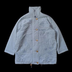 Peut inclure: Une veste matelassée bleu clair avec un col montant et des boutons dorés. La veste présente un design unique avec des détails brodés.