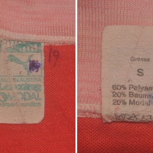 Op de afbeelding: Twee witte stoffen labels met zwarte tekst. Het label aan de linkerkant zegt "Made in Austria" en "Lenzig Modal" met een Puma-logo. Het label aan de rechterkant zegt "Grosse S" en "60% Polyamide 20% Katoen 20% Modal".