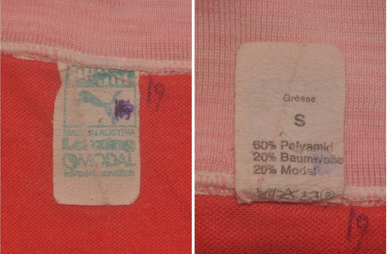Op de afbeelding: Twee witte stoffen labels met zwarte tekst. Het label aan de linkerkant zegt "Made in Austria" en "Lenzig Modal" met een Puma-logo. Het label aan de rechterkant zegt "Grosse S" en "60% Polyamide 20% Katoen 20% Modal".