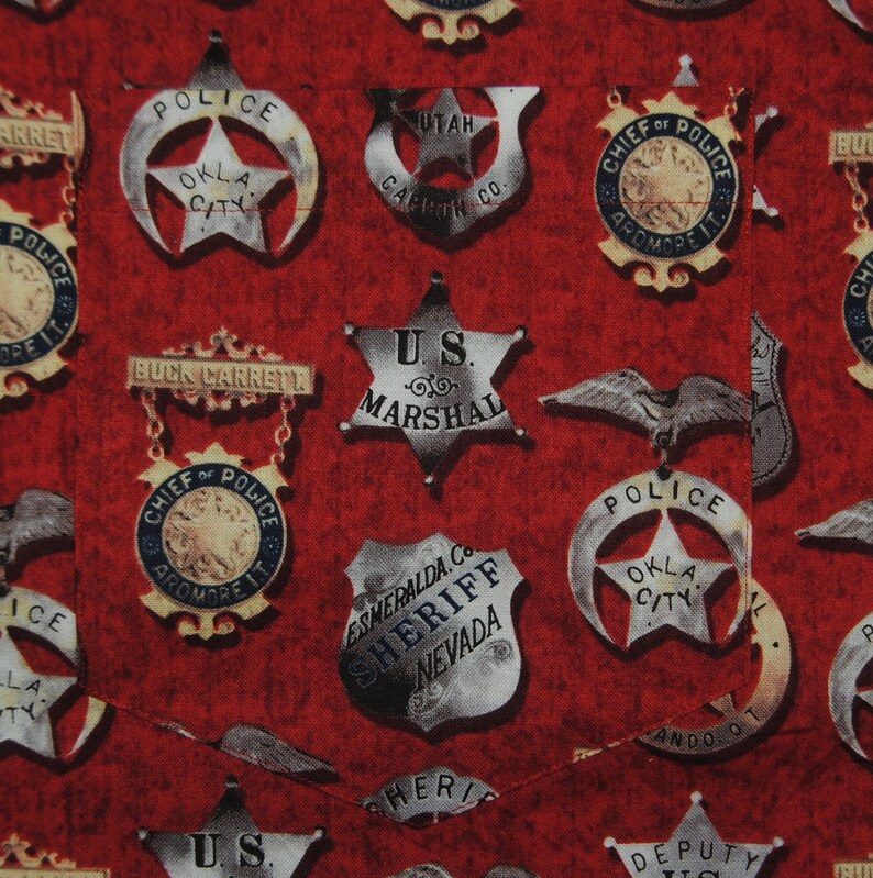 Pode incluir: Tecido vermelho com um padr&atilde;o de distintivos de pol&iacute;cia e xerife vintage. Os distintivos, em forma de estrela e escudo, trazem textos como "U.S. Marshal" e "Okla City Police".