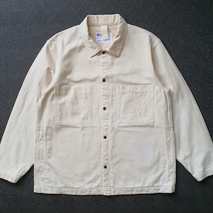May include: A light beige button-down shirt with two front pockets and a collar. The long-sleeved shirt has dark buttons and a small tag near the collar. The shirt is made of a sturdy fabric.
