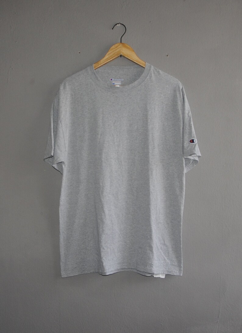 Op de afbeelding: Een grijs T-shirt met korte mouwen en een Champion-logo op de linkermouw.