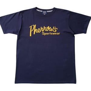 May include: A navy blue crew neck t-shirt featuring the text "Pherrow's Sportswear" in a yellow, cursive font. The shirt is made of a soft material and is laid flat. The overall design is simple and classic.
