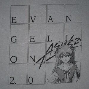 May include: A gray t-shirt with a black and white illustration of a character from the anime series Neon Genesis Evangelion. The illustration is superimposed over a grid with the letters "EVANGELION" written in the squares. The number "2.0" is written in the bottom left corner of the grid.