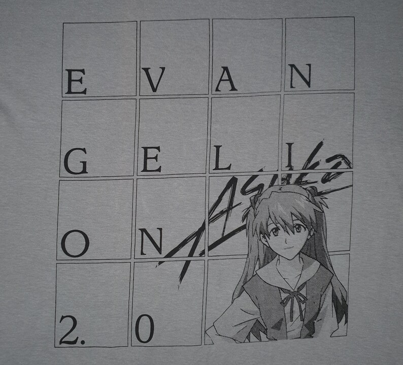 May include: A gray t-shirt with a black and white illustration of a character from the anime series Neon Genesis Evangelion. The illustration is superimposed over a grid with the letters "EVANGELION" written in the squares. The number "2.0" is written in the bottom left corner of the grid.