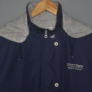 Puede incluir: Una chaqueta azul marino con capucha y forro de polar gris. La chaqueta tiene cierre de cremallera y solapa con botones. La chaqueta tiene el texto "courr&egrave;ges sport futur" en la parte delantera.