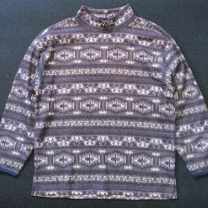 Op de afbeelding: Een grijze fleece trui met lange mouwen en een wit en grijs geometrisch patroon.