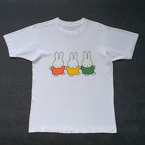 Puede incluir: Camiseta blanca con un gráfico de tres conejos de dibujos animados que llevan camisas de diferentes colores. Los conejos se toman de la mano y sonríen.