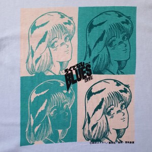 May include: A light blue t-shirt with a repeated image of a girl with long, dark hair. The image is in a teal and pink color scheme. The text "シティ・ブルース" and "BLUES 1993" is printed on the shirt.