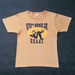 May include: A tan t-shirt with a black graphic of a plane and the text "670th BOMB. SQ. U.S.A.A.F."