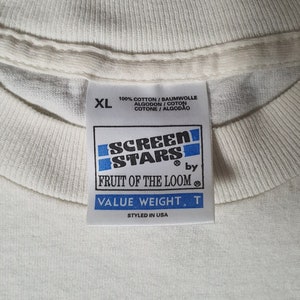 Pode incluir: Etiqueta de camiseta branca com texto azul e preto que diz "Screen Stars by Fruit of the Loom Value Weight. T Styled in USA". A etiqueta tamb&eacute;m diz "100% Algod&atilde;o/Baumwolle Algodon/Coton Cotone/Algodao" e tem uma etiqueta de tamanho que diz "XL".