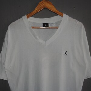 K&ouml;nnte beinhalten: Wei&szlig;es T-Shirt mit V-Ausschnitt und einem kleinen schwarzen Jumpman-Logo auf der Brust.