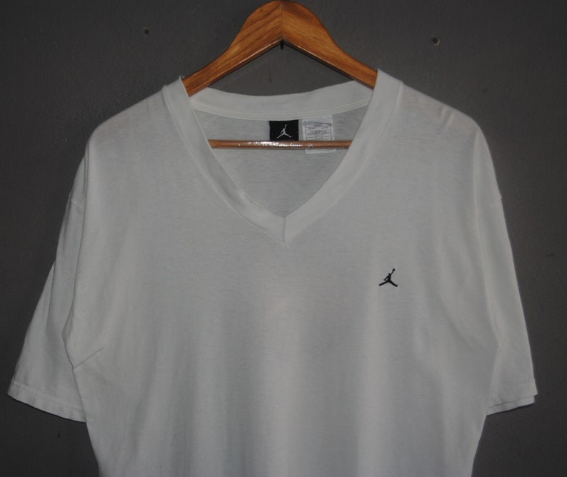 K&ouml;nnte beinhalten: Wei&szlig;es T-Shirt mit V-Ausschnitt und einem kleinen schwarzen Jumpman-Logo auf der Brust.