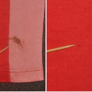 Op de afbeelding: Close-up van een rood en roze gestreepte stof met een bruine vlek op de roze kant. Een tandenstoker is op de stof geplaatst om de textuur te laten zien. De andere kant van de afbeelding toont een close-up van een rode stof met een kleine bruine vlek.