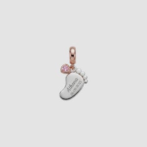 Può includere: Un charm in argento con un design a impronta di bambino. Il charm ha un anello in oro rosa e un accento a forma di cuore rosa. L'impronta è incisa con il nome "Athena" e la data "24/09/2025".