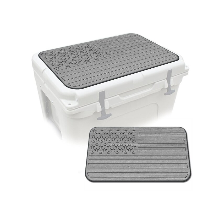 May include: A gray, American flag-themed cooler lid mat. The mat has a textured surface and is designed to fit on top of a cooler. The mat is shown on top of a white cooler and also separately.
