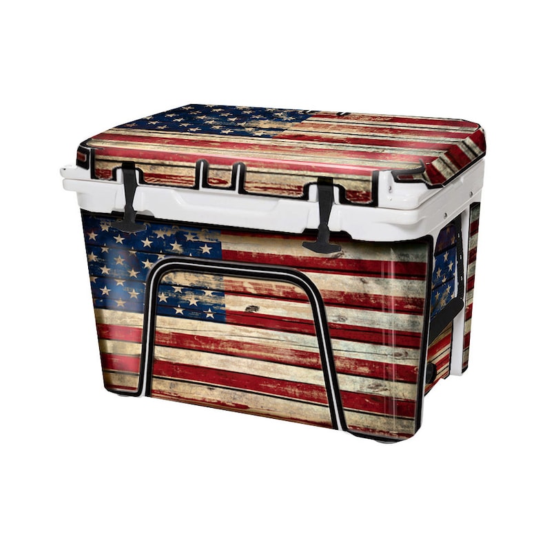 May include: A white cooler with a weathered American flag design. The cooler features a red, white, and blue flag print on a wooden plank background. It has a black handle and latches.