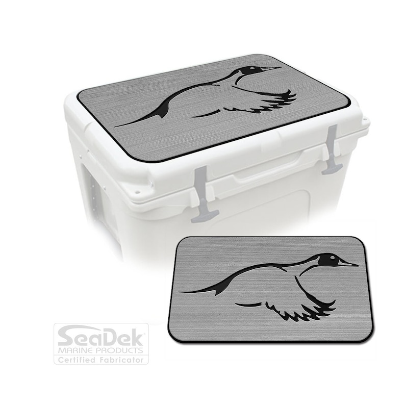 Pu&ograve; includere: Un refrigeratore bianco con un coperchio grigio con una silhouette nera di un'anatra in volo. Il coperchio ha un aspetto strutturato. Una versione pi&ugrave; piccola del coperchio &egrave; mostrata sotto. Prodotto da SeaDek Marine Products.