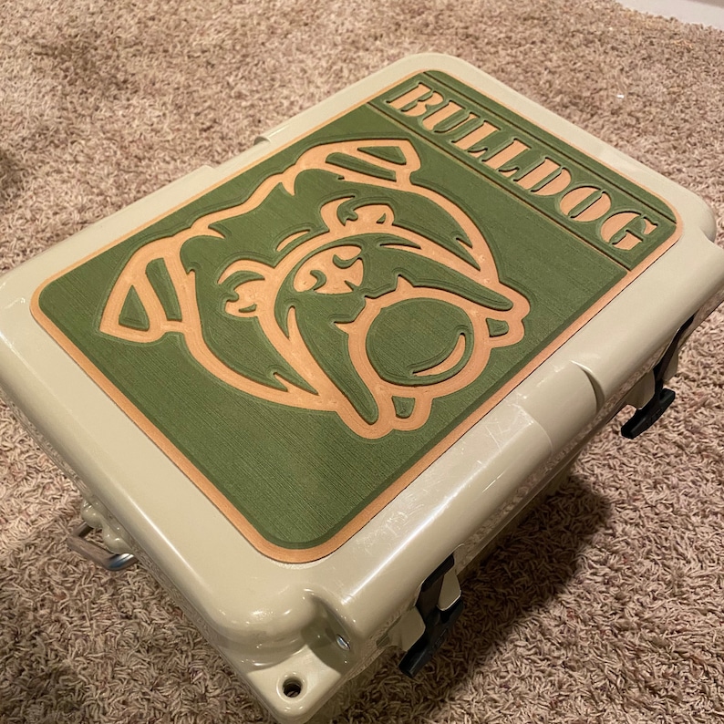 May include: A beige cooler with a green and brown bulldog graphic on the lid. The graphic says "Bulldog" in a brown font.
