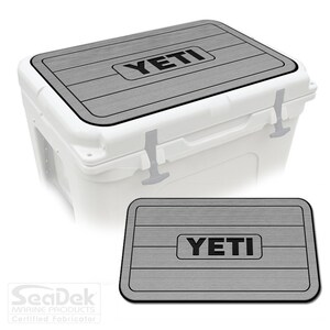 May include: Gray and black Yeti cooler lid and mat. The lid and mat have a wood-grain pattern and the Yeti logo is printed in black.