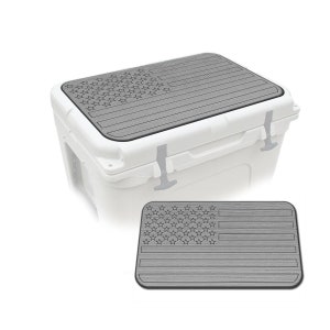 May include: A white cooler with a gray lid featuring an American flag design. The flag design is etched into the lid, and a separate flag-designed pad is shown below the cooler.