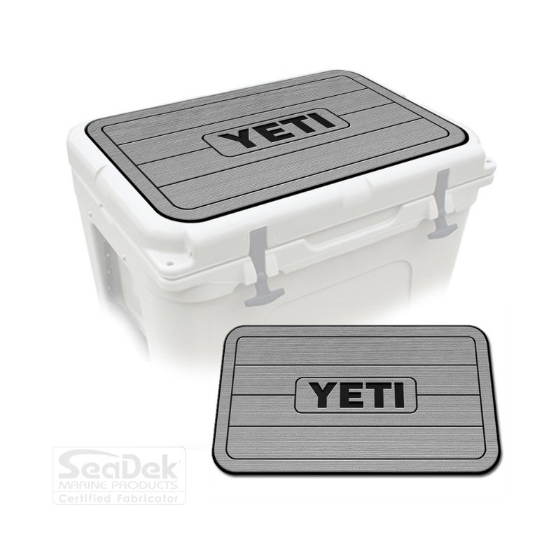 May include: Gray and black SeaDek non-slip cooler lid mat with the word "YETI" printed on it. The mat is designed to fit on top of a YETI cooler.