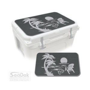 May include: White cooler with a dark grey lid featuring a beach scene design. The design includes a palm tree, sun, ocean, and a beach chair. The cooler has grey latches and the SeaDek Marine Products logo.