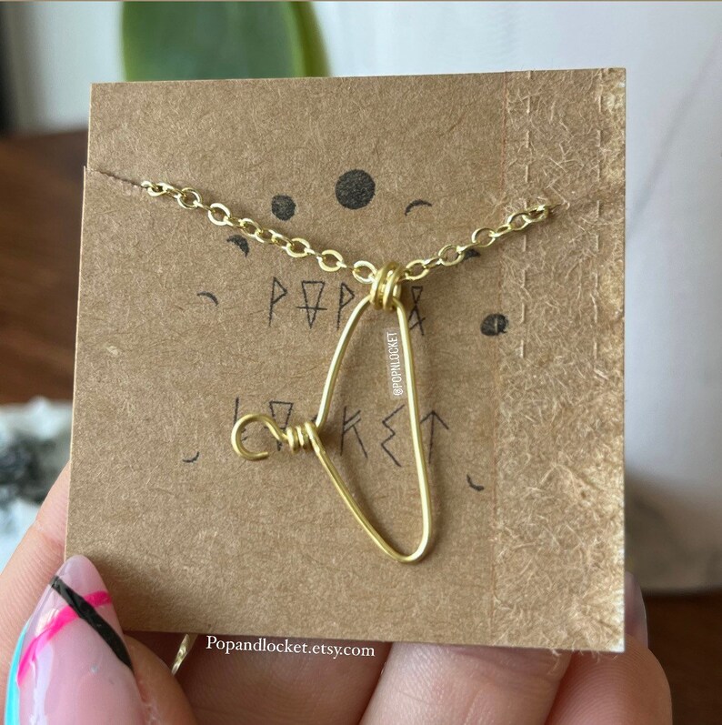 May include: A gold necklace with a heart-shaped pendant made of wire. The pendant is on a card with the text "Pop & Locket" and the social media handle "@popandlocket".