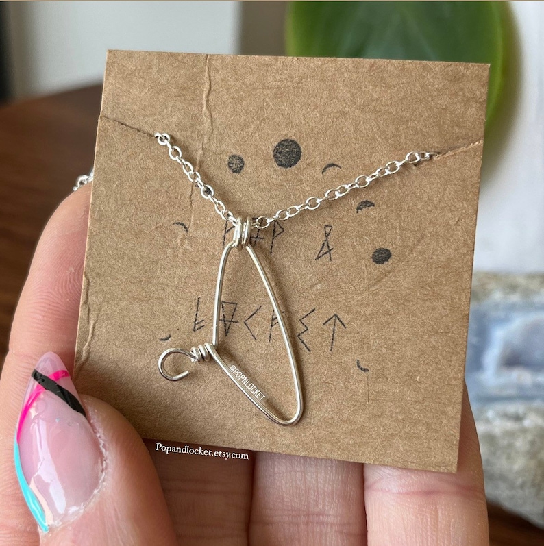 May include: A silver necklace with a triangle pendant. The pendant is made of wire and has a small loop at the top. The necklace is on a brown card with the text "Popandlocket.etsy.com" and "@popandlocket".