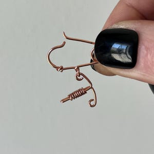 May include: Rose gold wire earrings with a coiled wire design. The earrings have a hook closure.