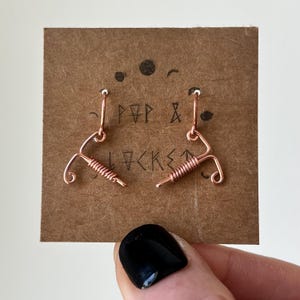 May include: A pair of copper wire earrings shaped like an IUD. The earrings are on a brown card with the text "POP & LOCKED" written on it.