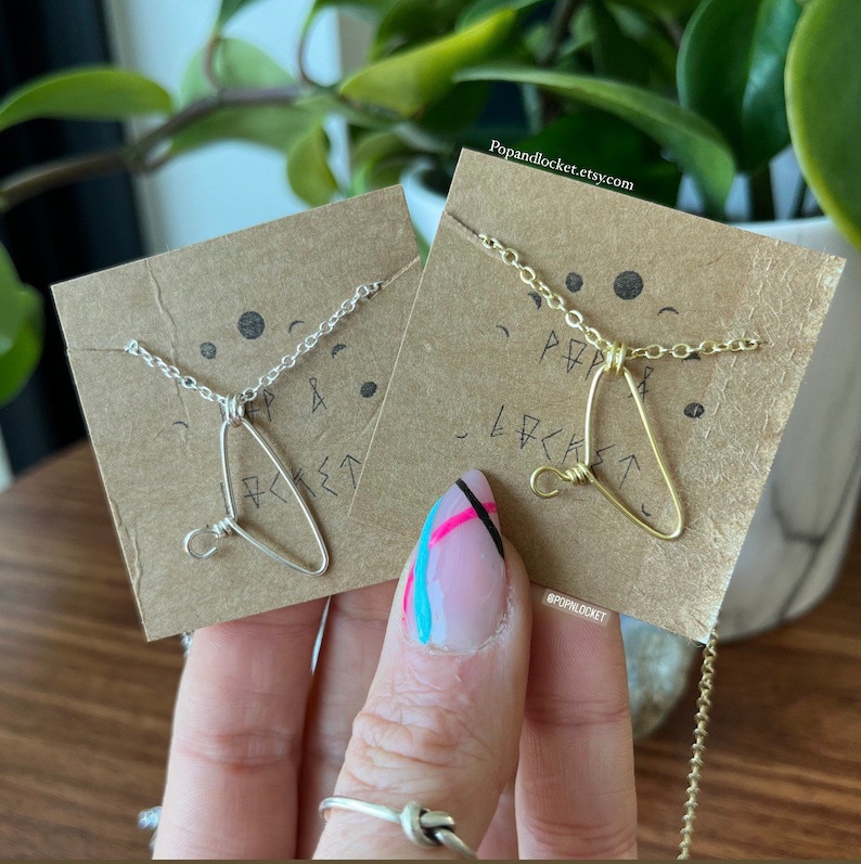 May include: Two necklaces with triangle pendants on brown card stock. The necklaces are silver and gold. The card stock has the text "Popandlocket.etsy.com" and "#popandlocket".