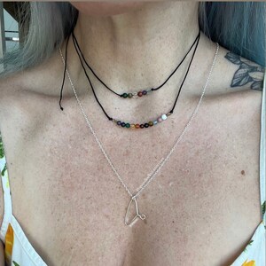May include: A silver necklace with a letter 'L' pendant and two layered necklaces with colorful gemstone beads.