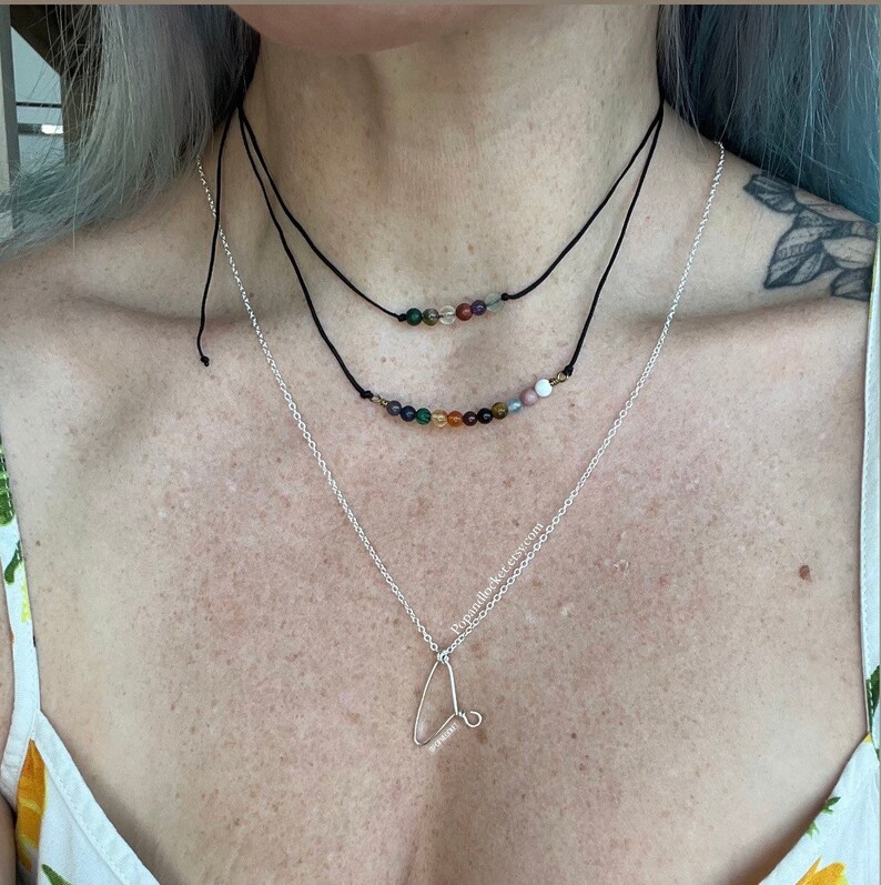 May include: A silver necklace with a letter 'L' pendant and two layered necklaces with colorful gemstone beads.