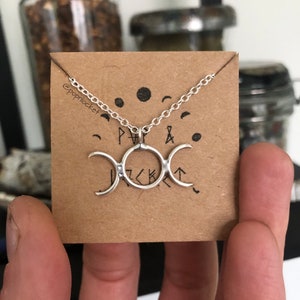 May include: Silver triple moon necklace with a chain on a brown card with the text "@popplacket" and symbols.