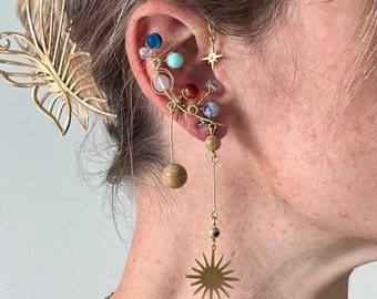 May include: Gold ear cuff with multiple charms, including a star, a wooden bead, and various gemstones. The ear cuff is worn on the left ear.