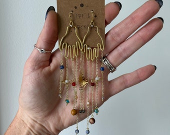 May include: Gold hand-shaped earrings with dangling chains and colourful beads, including planets and stars. The earrings are labelled "PPP & P<K>"