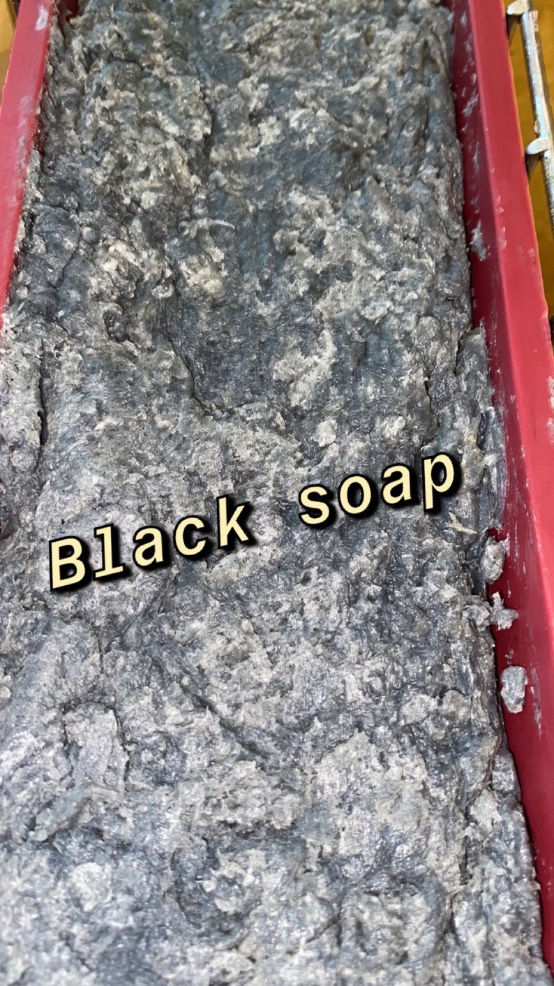 Op de afbeelding: Een close-up van een donkergrijze, getextureerde zeepstaaf in een rode siliconen mal. De zeep is gelabeld met "Black soap".