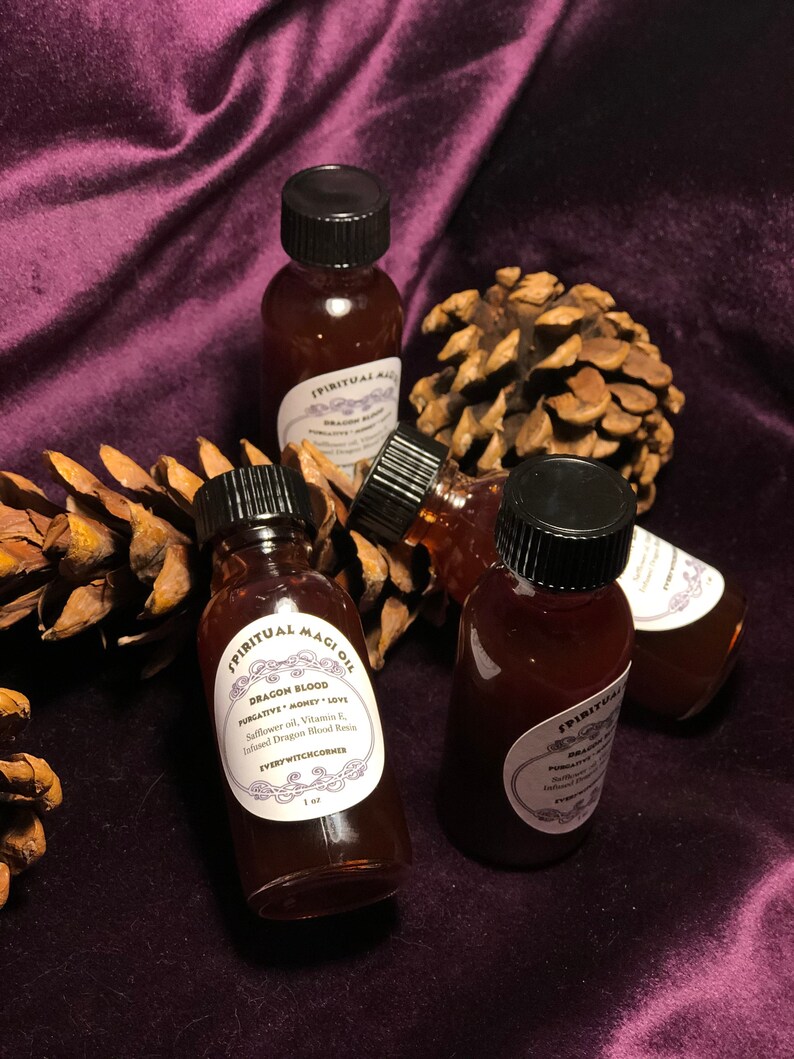 May include: Four small glass bottles with brown liquid and black lids. The bottles are labeled "SPIRITUAL MAGIOIL" and "DRAGON BLOOD PURGATIVE MONEY LOVE" with the text "Safflower oil, Vitamin E, Infused Dragon Blood Resin" and "EVERY WITCHCORNER 1 oz". The bottles are sitting on a brown pine cone and a purple velvet surface.