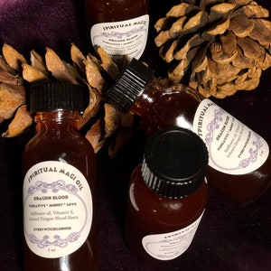 May include: Four small glass bottles with black lids filled with a dark red liquid. Each bottle has a white label with black text that reads "SPIRITUAL MAGI OIL" and "DRAGON BLOOD PURGATIVE MONEY LOVE Safflower oil, Vitamin E, Infused Dragon Blood Resin EVERYWITCHCORNER 1 oz".