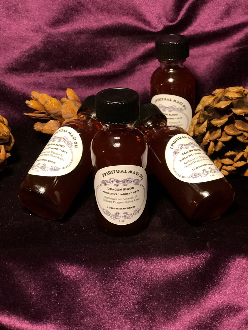 May include: Six small bottles of dark red liquid with black lids and white labels. The labels say "Spiritual Magick Oil" and "Dragon Blood" with the words "Purgative, Money, Love" underneath. The bottles are on a purple velvet surface.