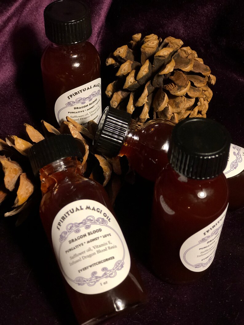 May include: Three small glass bottles filled with a dark red liquid. The bottles have black caps and white labels with the text "SPIRITUAL MAGIOIL DRAGON BLOOD PURGATIVE MONEY LOVE Safflower oil, Vitamin E, Infused Dragon Blood Resin EVERY WITCHCORNER 1 oz" printed on them.