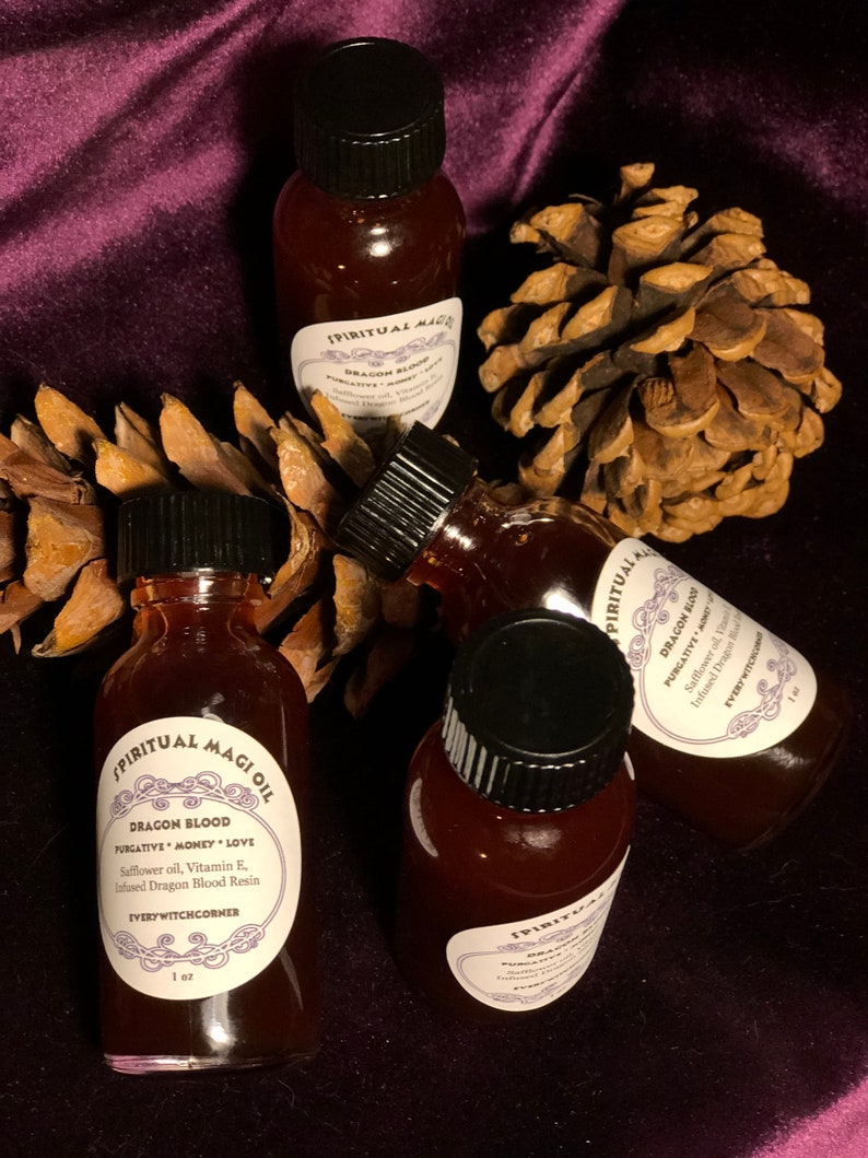 May include: Four small glass bottles with black caps filled with a dark red liquid. Each bottle has a white label with black text that reads "SPIRITUAL MAGI OIL" and "DRAGON BLOOD PURGATIVE MONEY LOVE" with additional details about the ingredients. The bottles are arranged on a brown pine cone and a purple velvet background.