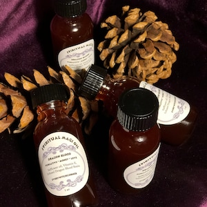 May include: Four small glass bottles filled with a dark red liquid. The bottles have black caps and white labels with the text "SPIRITUAL MAGI OIL" and "DRAGON BLOOD" on them. The bottles are sitting on a brown pine cone and a purple velvet surface.