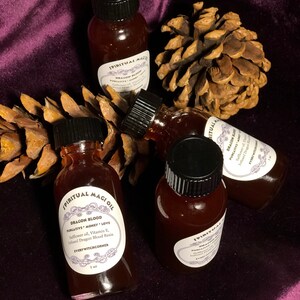 May include: Four small glass bottles with black caps filled with a dark red liquid. The bottles are labeled "Spiritual Magic Oil" and "Dragon Blood Purgative Money Love". The bottles are sitting on a brown pine cone and a purple velvet surface.