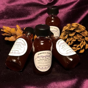 May include: Four small brown glass bottles with black caps filled with a dark red liquid. Each bottle has a white label with black text that reads "Spiritual Magic Oil" and "Dragon Blood Purgative Money Love Safflower oil, Vitamin E, Infused Dragon Blood Resin EveryWitchCorner 1 fl oz".