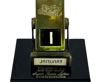 Pode incluir: Um calendário de mesa vintage verde e dourado com uma base preta. O calendário apresenta o texto "JANUARY" e "INDIA Super Foam Latex CUSHIONING".