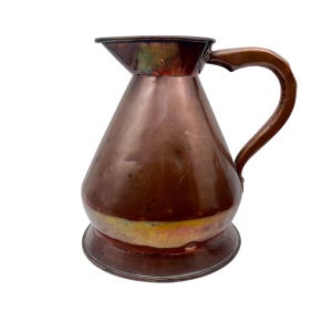 May include: A copper pitcher with a wide base and a narrow spout. The pitcher has a curved handle and a polished finish. The copper has a warm, reddish-brown hue with some areas of tarnish. The pitcher is likely an antique or vintage item.